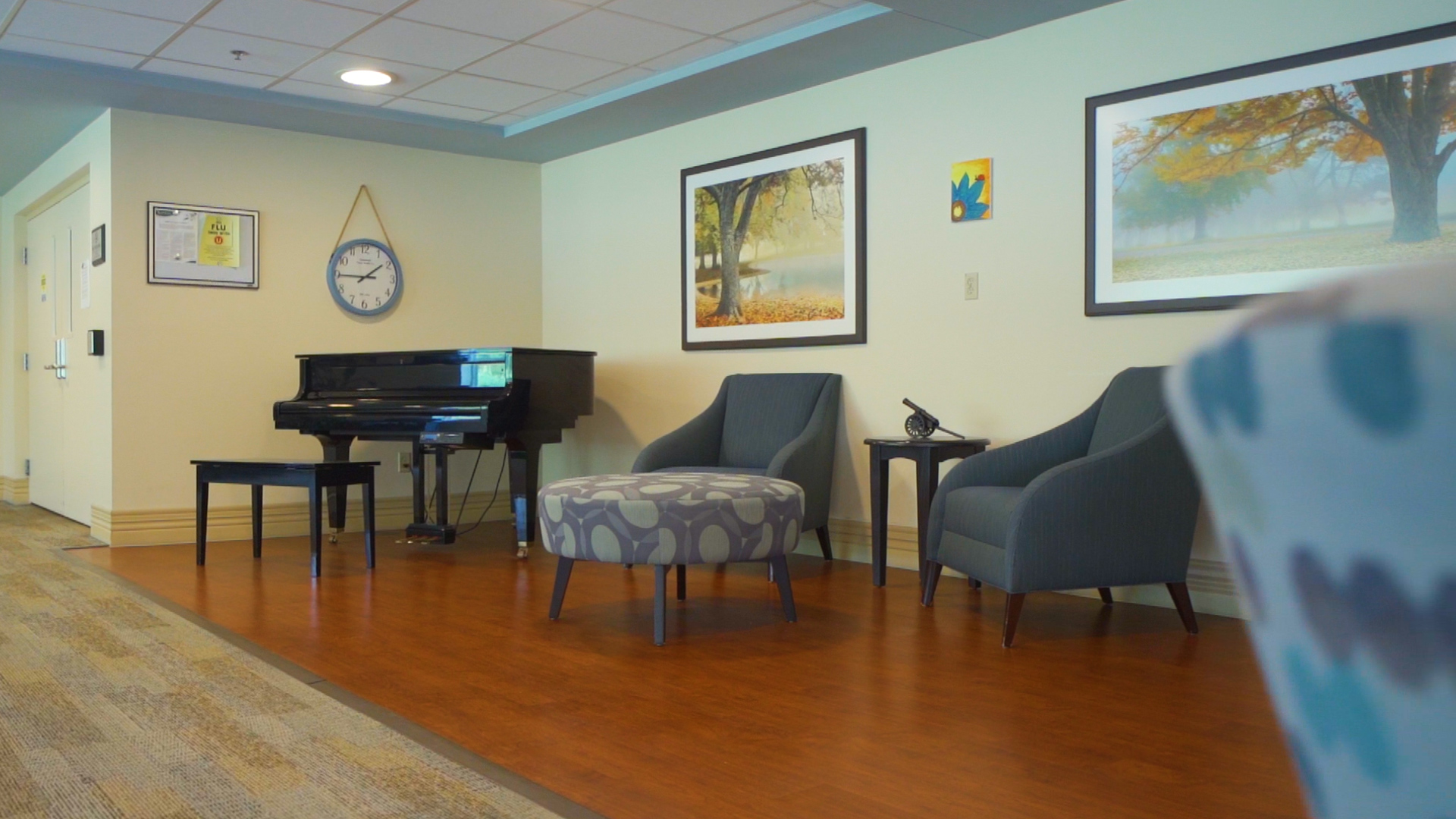 Black Piano with sofa and mini table on the side. Picture frames and a clock on the wall.